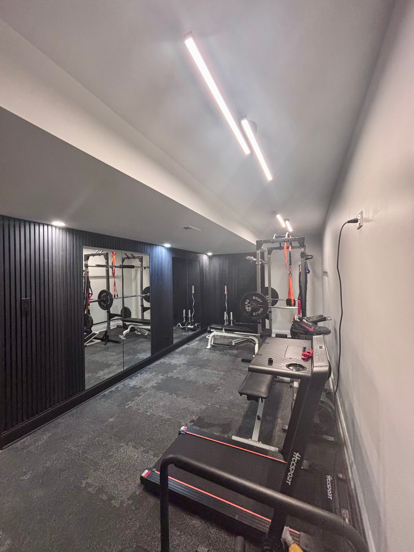 Home gym with black slat walls, mirrors and free weights