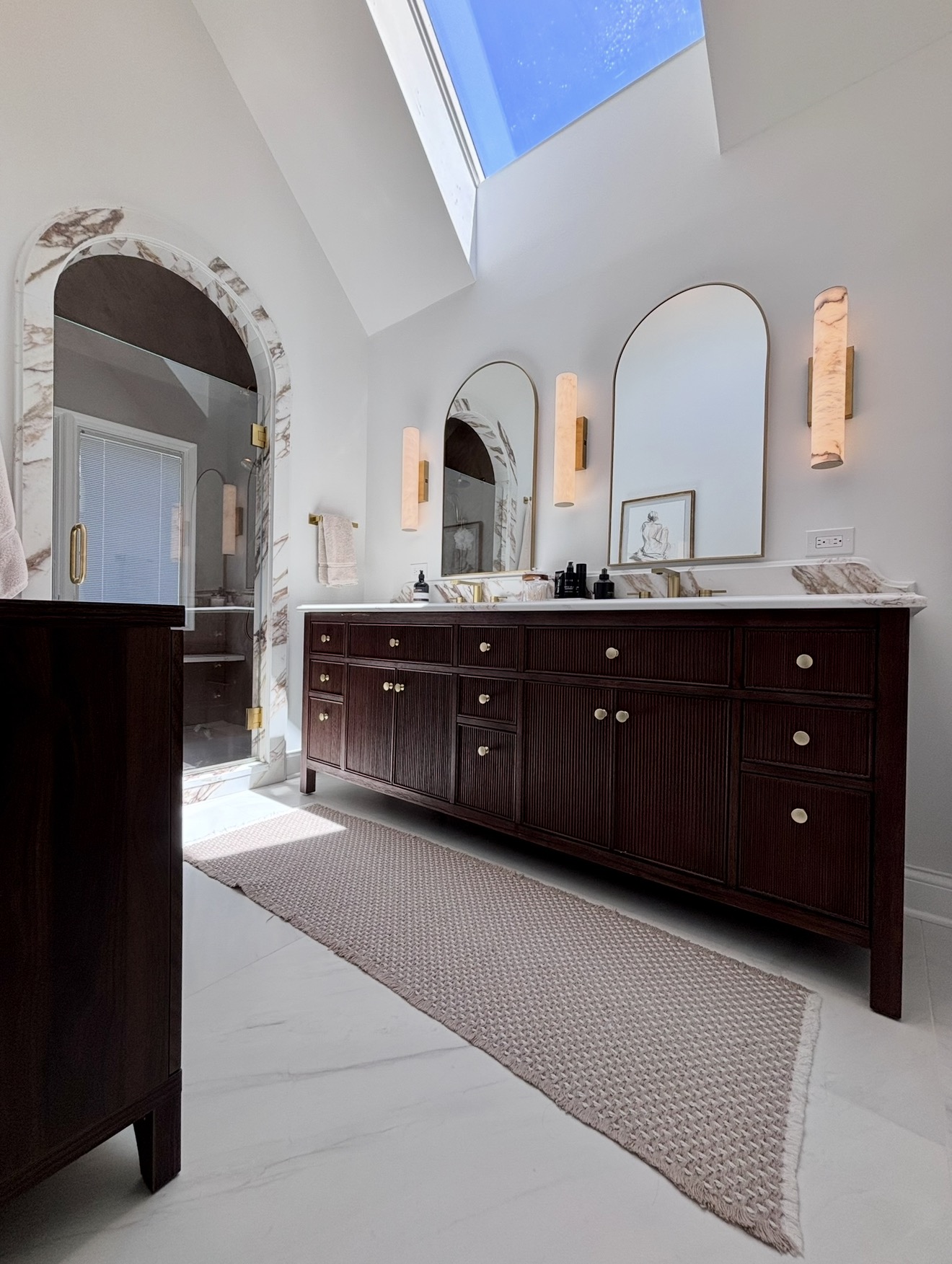 Vaulted master bath with skylight, dark vanity and arched mirrors