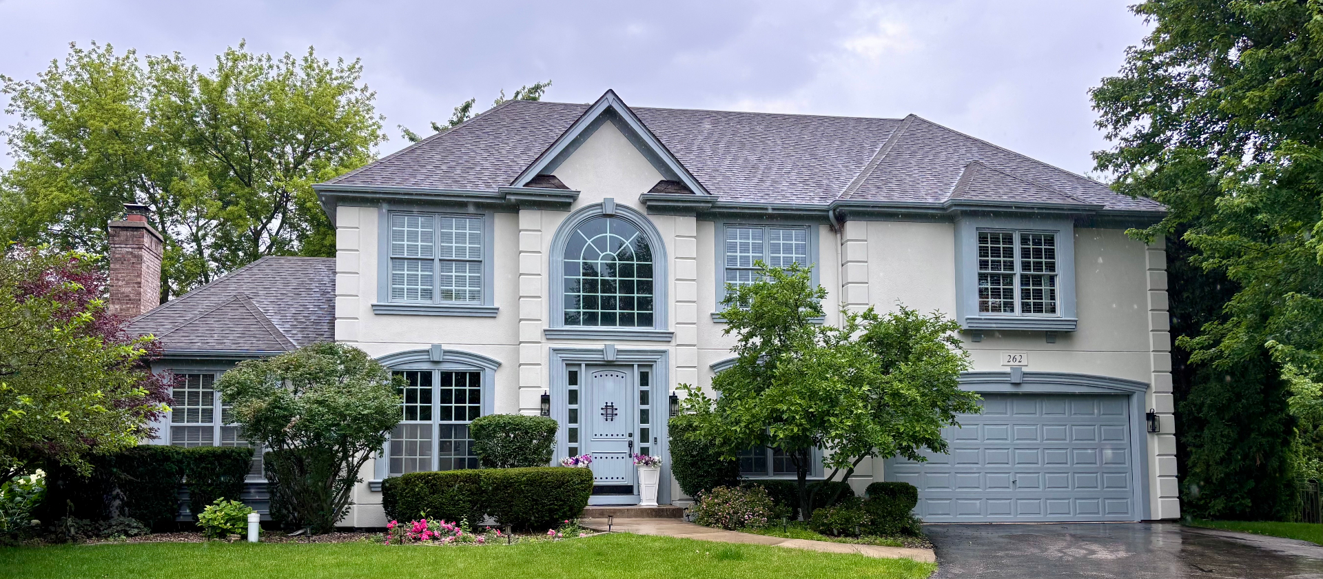 Front exterior of a stucco custom home with blue-grey trim and manicured landscaping