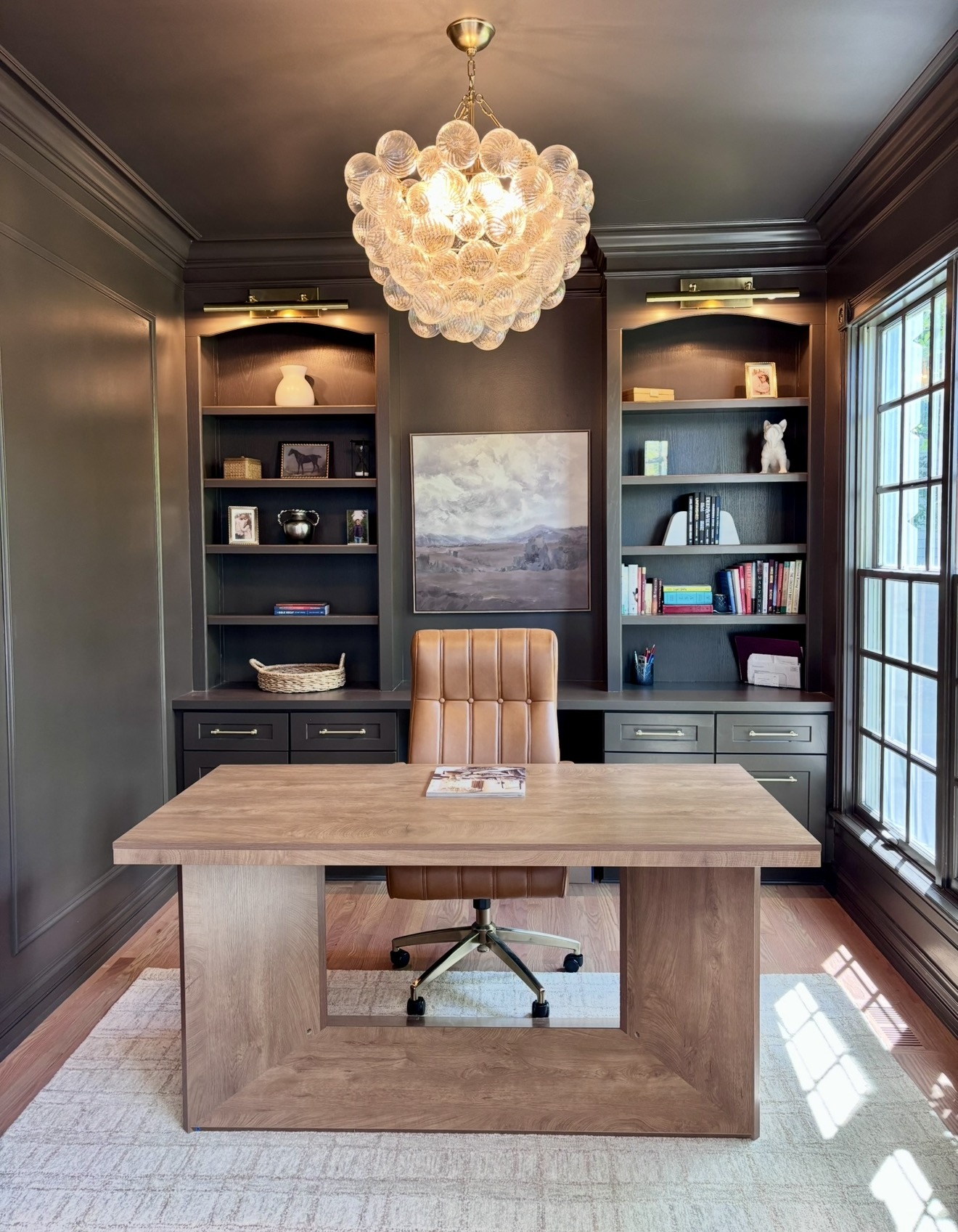 Home office with dark green built-ins and glass chandelier